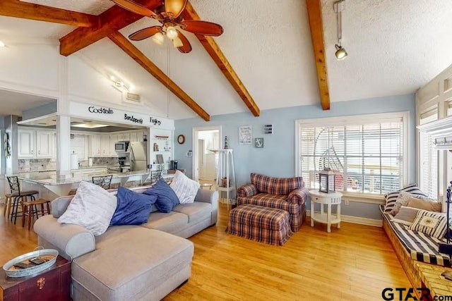 living area with light wood finished floors, lofted ceiling with beams, ceiling fan, a textured ceiling, and baseboards