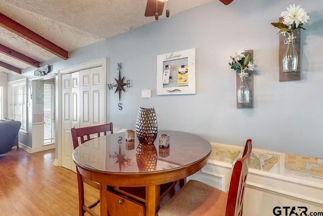 dining area with a textured ceiling, beamed ceiling, a ceiling fan, and light wood-style floors