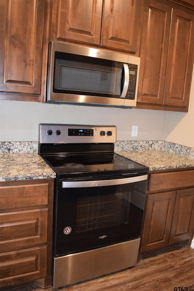 kitchen with dark hardwood / wood-style floors, light stone counters, and appliances with stainless steel finishes