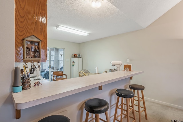 kitchen featuring a textured ceiling, baseboards, light colored carpet, and a kitchen breakfast bar