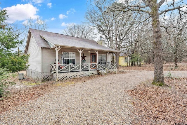 view of front facade with a porch, central AC unit, driveway, roof with shingles, and a chimney