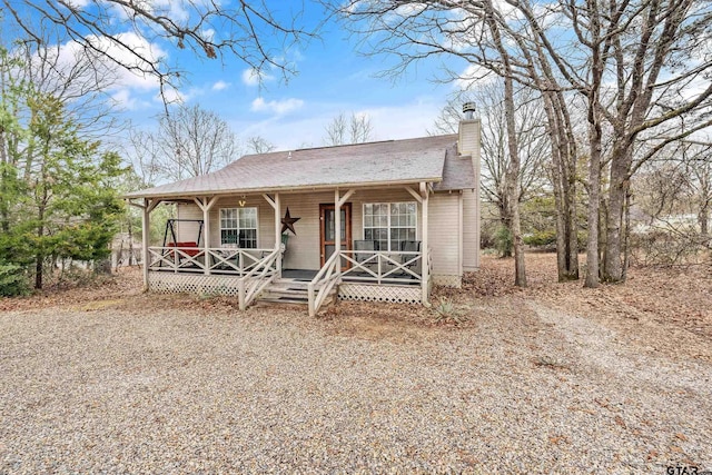 view of front facade with covered porch, driveway, and a chimney