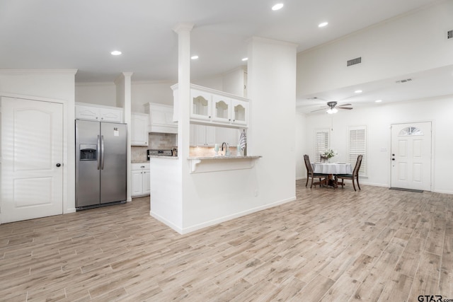 kitchen with light hardwood / wood-style floors, vaulted ceiling, white cabinets, kitchen peninsula, and stainless steel fridge