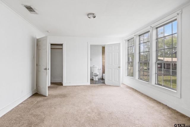 unfurnished bedroom with carpet flooring, connected bathroom, visible vents, and ornamental molding