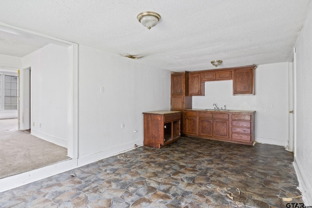 kitchen with stone finish floor, baseboards, a textured ceiling, a sink, and brown cabinets