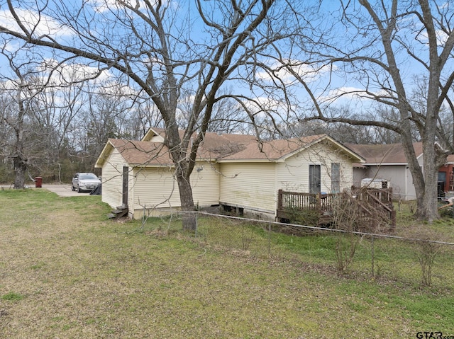 view of side of property with a wooden deck, roof with shingles, fence, and a lawn