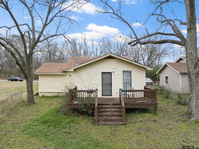 back of property with a shingled roof, a lawn, a wooden deck, and fence