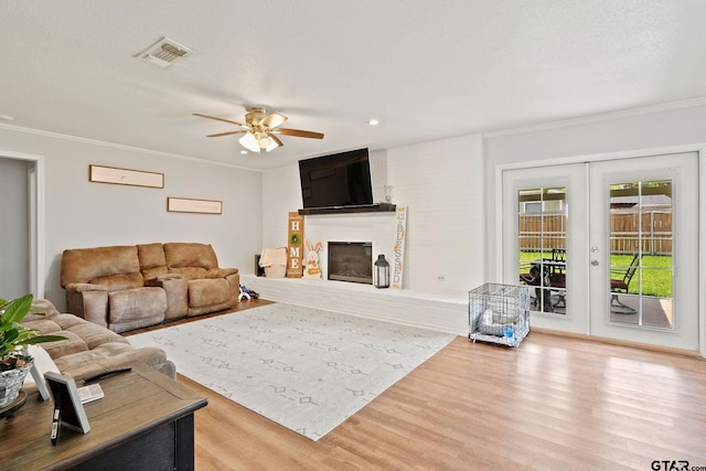 living area featuring visible vents, a ceiling fan, wood finished floors, a fireplace, and ornamental molding