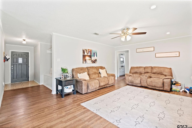 living area featuring wood finished floors, visible vents, a ceiling fan, crown molding, and baseboards