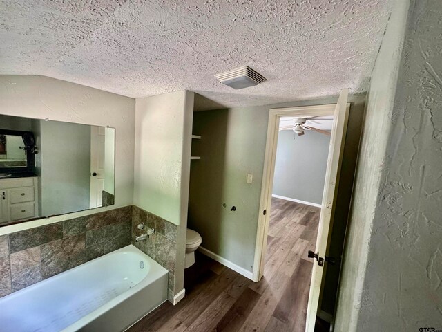 bathroom featuring wood-type flooring, toilet, a textured ceiling, ceiling fan, and a tub to relax in