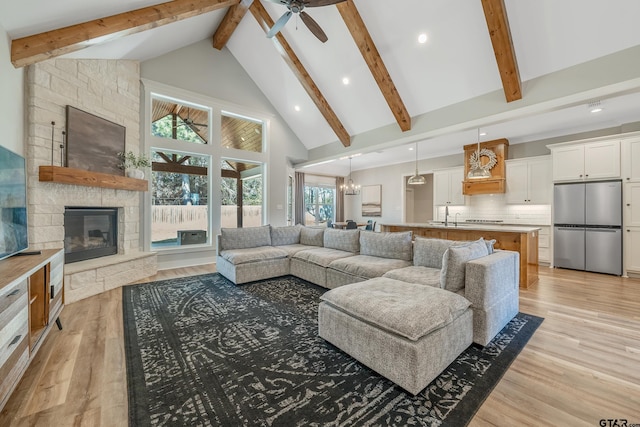 living area with beam ceiling, a fireplace, light wood finished floors, high vaulted ceiling, and ceiling fan with notable chandelier