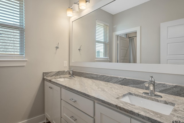 full bathroom with double vanity, baseboards, and a sink