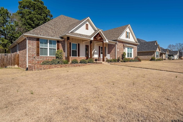 view of front of property featuring a shingled roof, a front yard, brick siding, and fence