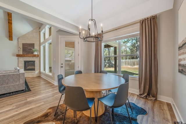 dining space featuring lofted ceiling with beams, light wood-style flooring, a fireplace, baseboards, and an inviting chandelier