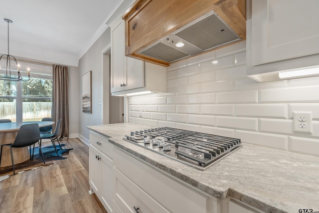 kitchen featuring stainless steel gas stovetop, premium range hood, hanging light fixtures, and white cabinets