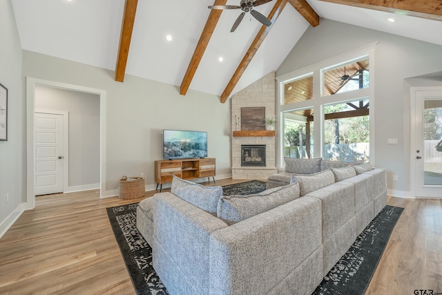 living room with high vaulted ceiling, beamed ceiling, a stone fireplace, and light wood finished floors