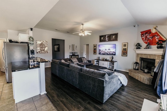 living room featuring a brick fireplace, vaulted ceiling, tile patterned floors, and ceiling fan