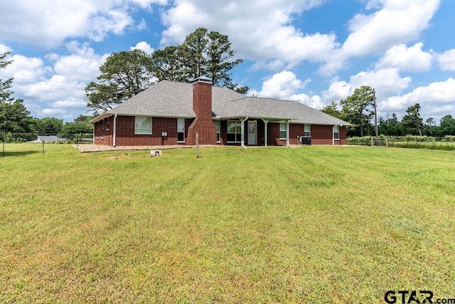 back of property featuring a lawn, a chimney, fence, and brick siding