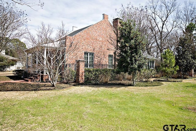 view of side of home with a yard, brick siding, and a chimney