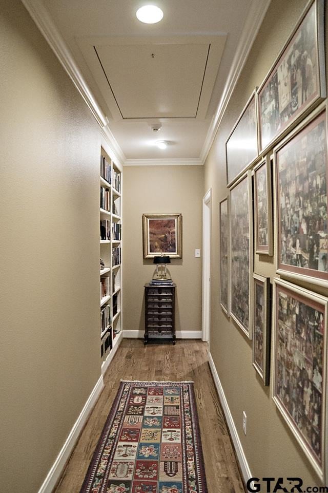 hallway with built in features, wood finished floors, baseboards, attic access, and ornamental molding