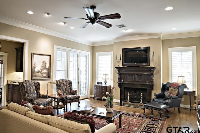 living room with a fireplace, crown molding, wood finished floors, and visible vents