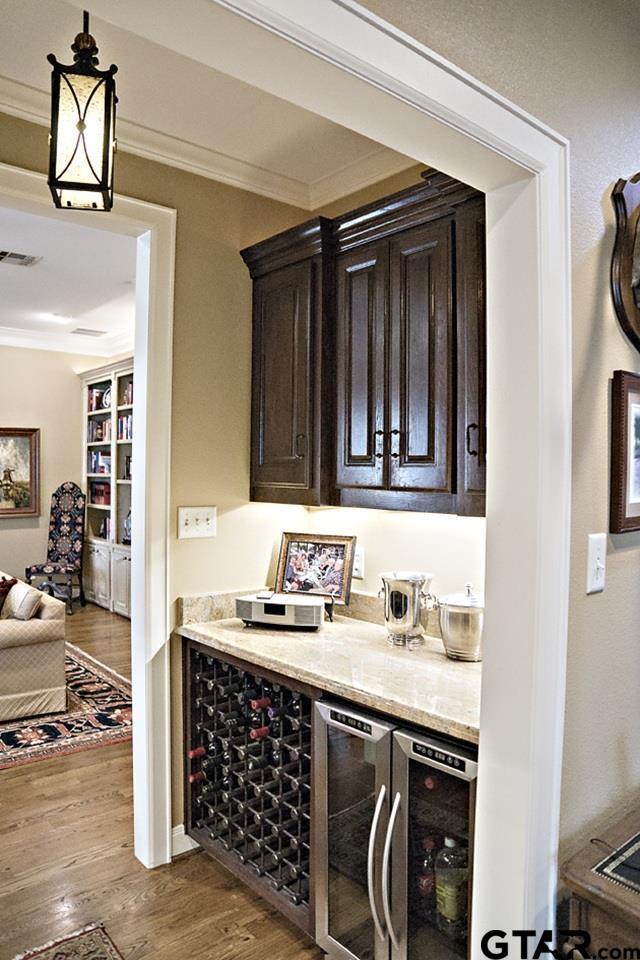 bar with wood finished floors, beverage cooler, visible vents, ornamental molding, and a bar