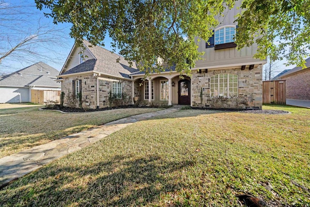 traditional-style house featuring board and batten siding, stone siding, fence, and a front lawn