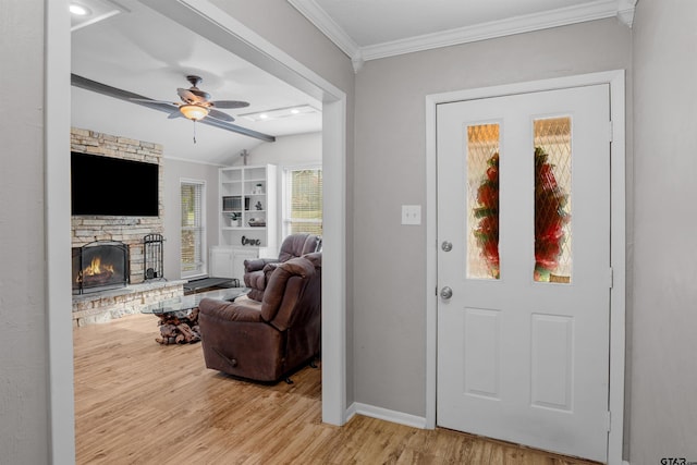 entryway featuring ceiling fan, a fireplace, ornamental molding, and light wood-type flooring