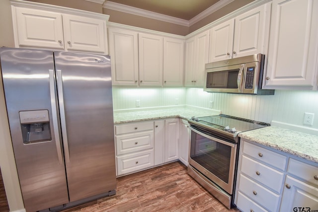 kitchen with appliances with stainless steel finishes, white cabinetry, wood-type flooring, ornamental molding, and light stone counters