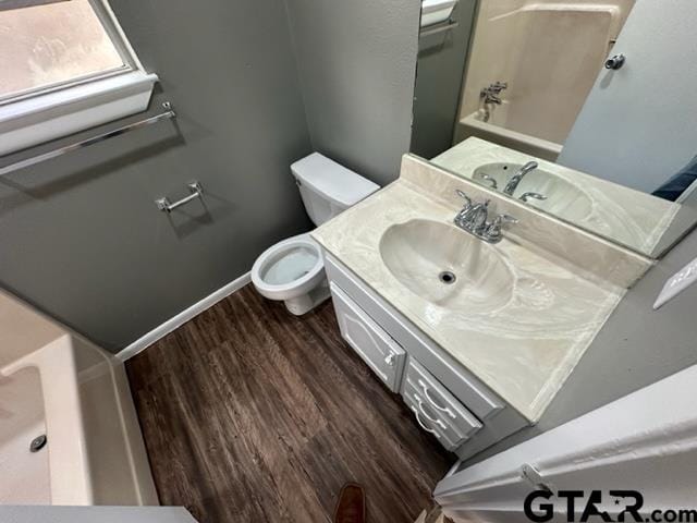 bathroom featuring baseboards, toilet, a tub to relax in, wood finished floors, and vanity