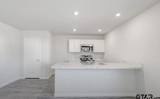 208 Parker Oaks Dr, Chandler, TX 75758 - kitchen featuring stainless steel microwave, stove, white cabinets, a peninsula, and baseboards