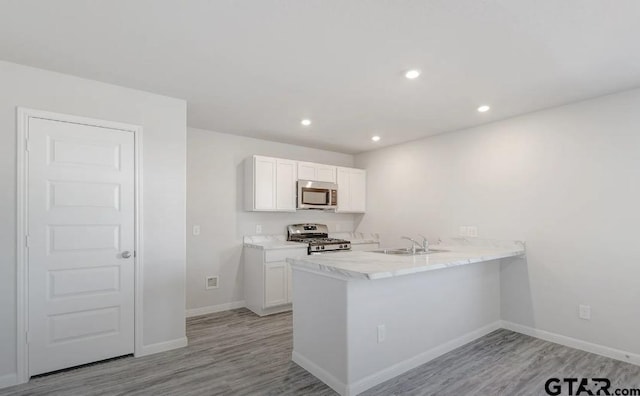 208 Parker Oaks Dr, Chandler, TX 75758 - kitchen featuring appliances with stainless steel finishes, a sink, white cabinets, a peninsula, and light wood finished floors