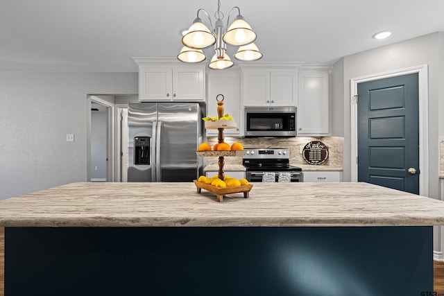 kitchen with pendant lighting, backsplash, stainless steel appliances, and white cabinets