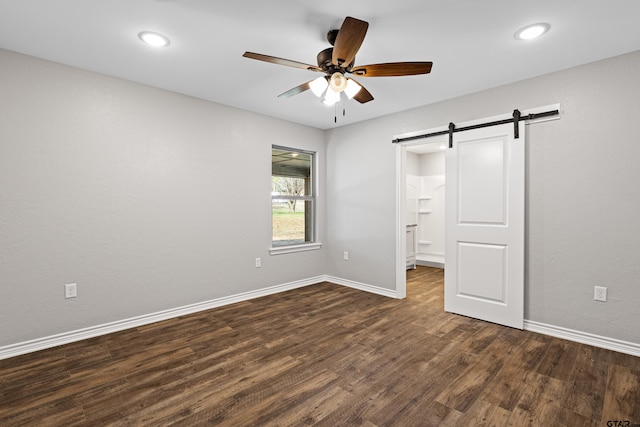 unfurnished bedroom with a barn door, dark hardwood / wood-style floors, and ceiling fan