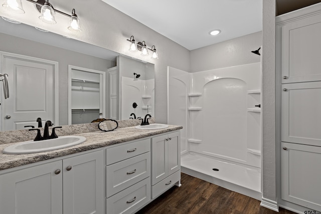 full bathroom with double vanity, wood finished floors, a sink, and a walk in shower