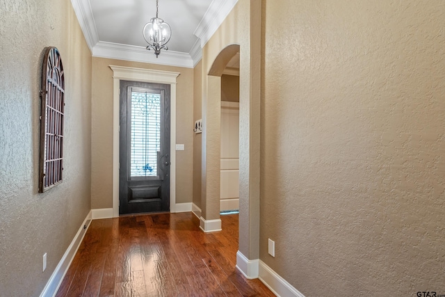 foyer entrance featuring a textured wall, arched walkways, ornamental molding, dark wood-style flooring, and a chandelier
