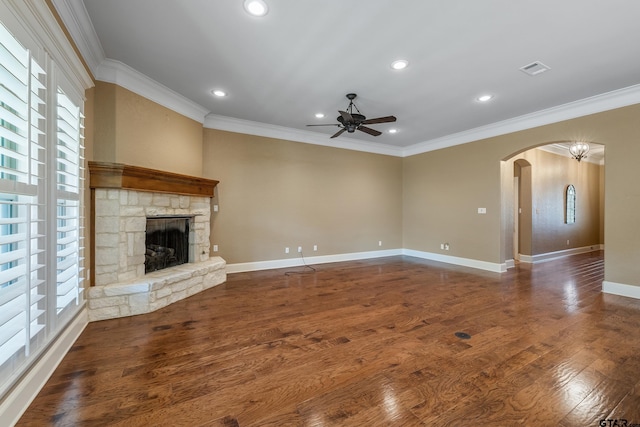 unfurnished living room featuring crown molding, arched walkways, a ceiling fan, a stone fireplace, and baseboards