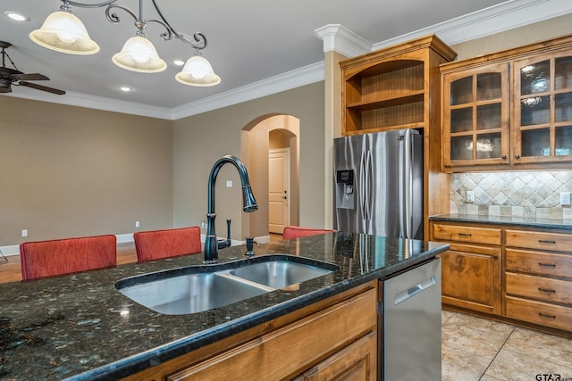 kitchen with appliances with stainless steel finishes, a sink, arched walkways, ornamental molding, and brown cabinetry
