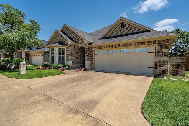 view of front of house featuring brick siding, an attached garage, a shingled roof, driveway, and a front lawn