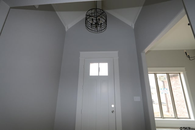 foyer entrance featuring crown molding, a chandelier, vaulted ceiling, and a wealth of natural light