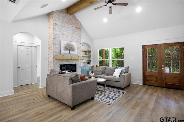 living area with a ceiling fan, a fireplace, beam ceiling, light wood-style flooring, and high vaulted ceiling