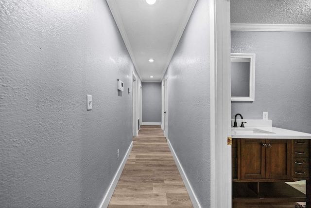 hallway with crown molding, sink, and light wood-type flooring