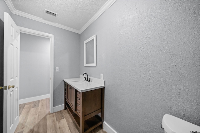 bathroom featuring crown molding, a textured ceiling, toilet, vanity, and hardwood / wood-style flooring