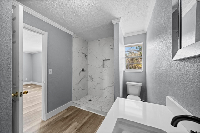 bathroom with hardwood / wood-style floors, toilet, ornamental molding, tiled shower, and a textured ceiling