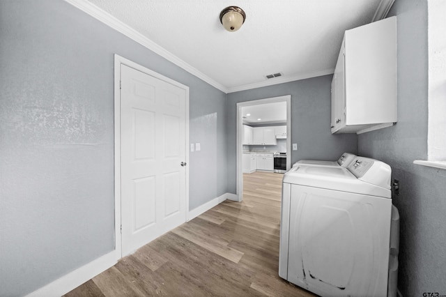 clothes washing area with washing machine and clothes dryer, crown molding, light hardwood / wood-style flooring, and cabinets