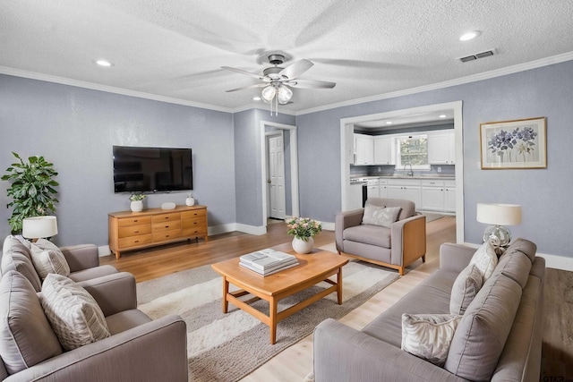 living room featuring ceiling fan, ornamental molding, a textured ceiling, and light hardwood / wood-style flooring