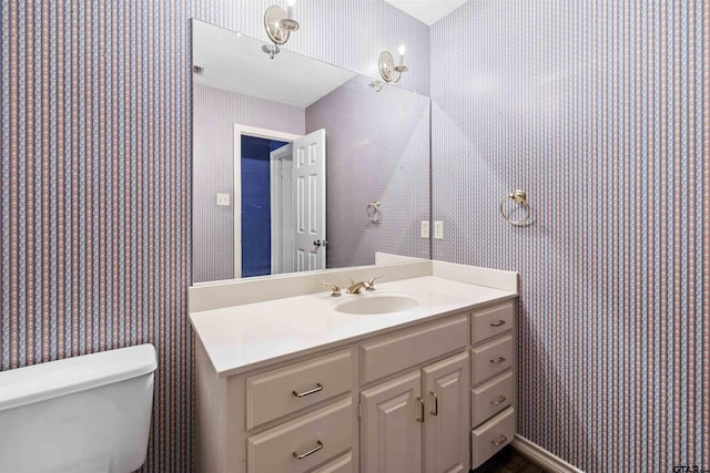 half bath featuring wallpapered walls, toilet, and vanity