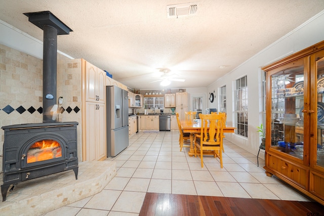 dining room with ceiling fan, light tile patterned floors, a wood stove, and a textured ceiling