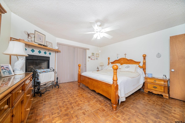 bedroom featuring parquet floors, ceiling fan, a tile fireplace, and a textured ceiling