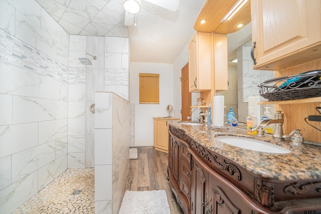 bathroom featuring wood-type flooring, vanity, a textured ceiling, tiled shower, and ceiling fan